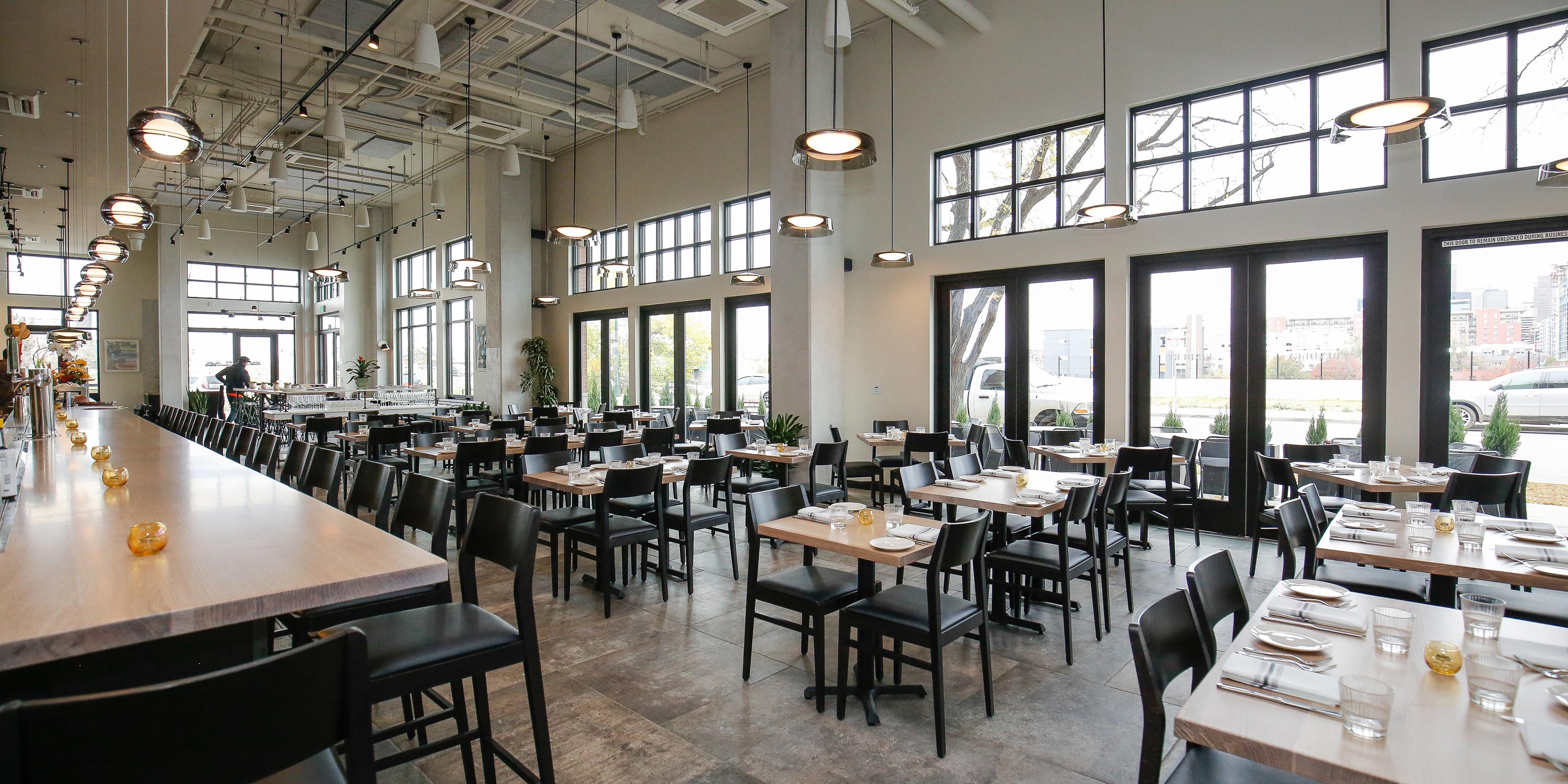 Bright restaurant interior with bar seating, dining tables, and large windows