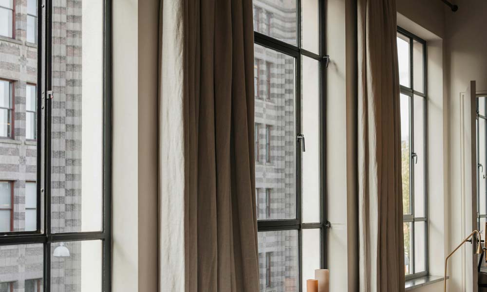 Tall loft windows with brown curtains in urban apartment