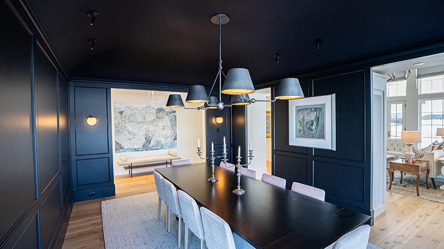 Dark dining room with black paneled walls, long table, modern chandelier, and framed artwork