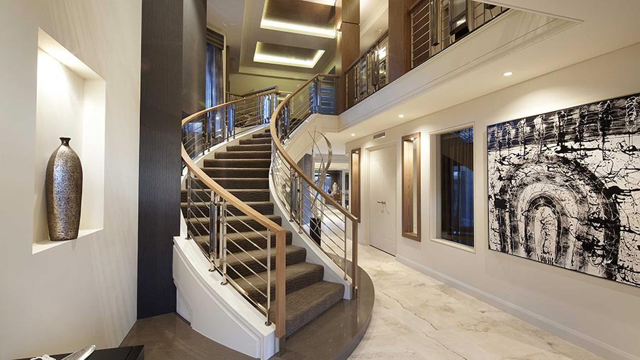Curved staircase in a luxury home with modern railing, marble floors, and large artwork