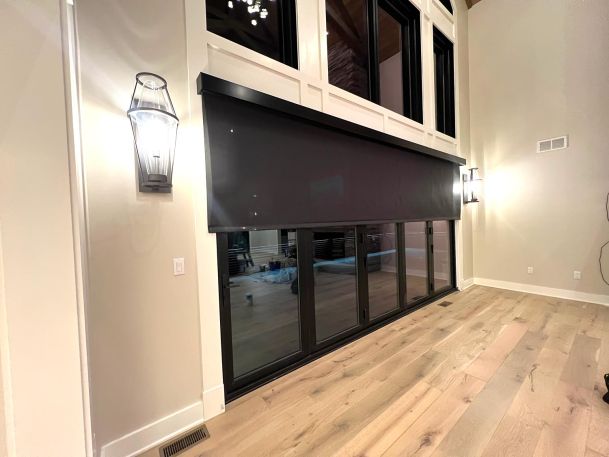 High ceiling room showing wide automated black out shade covering a multi panel glass door