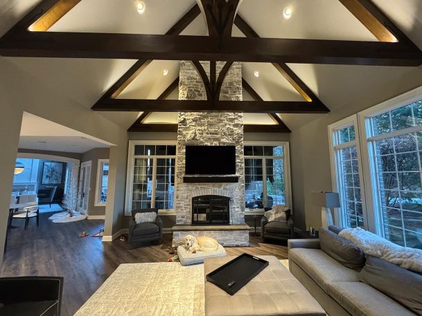 Cozy living room with stone fireplace under vaulted wood truss ceiling with warm lights