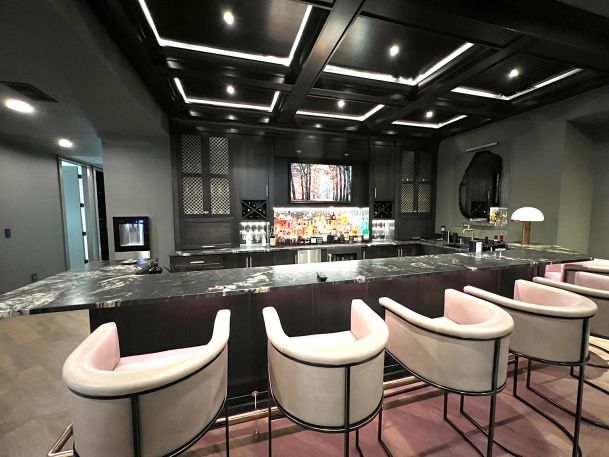Luxury home bar area featuring illuminated liquor shelves and black marble counters