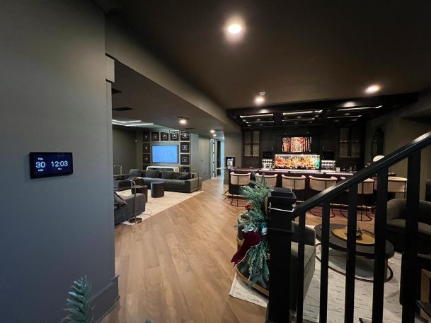 Home automation control monitor on gray wall showing time and date in a dark lounge room