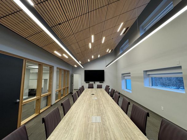 Long wooden boardroom table beneath linear hanging lights and sloped ceiling