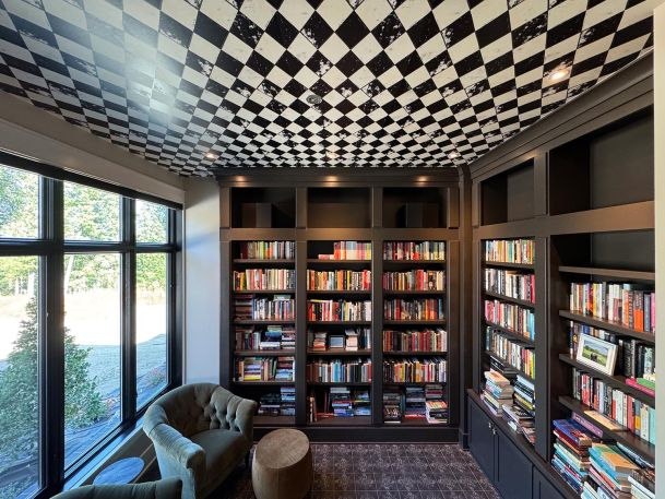 Home library with floor to ceiling dark wood bookcases and checkered pattern ceiling wallpaper