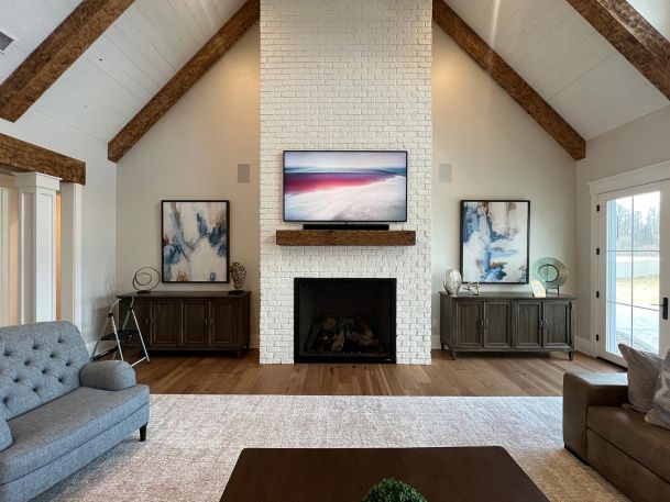 Bright living room with white brick fireplace and high vaulted ceiling with wood beams