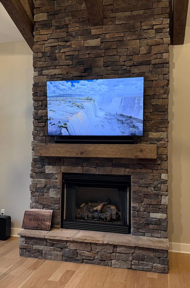Flat screen television over a stone fireplace displaying a waterfall screensaver image