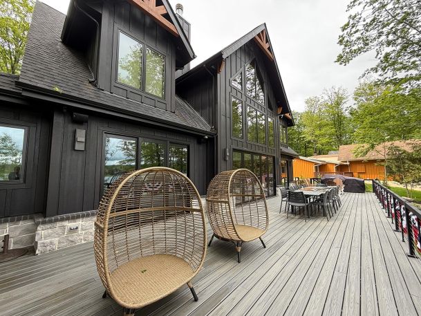 Modern black wood house showing large back deck patio with outdoor speakers and furniture