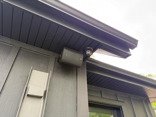 Exterior speaker and dome camera tucked under dark gray soffit corner of a house structure