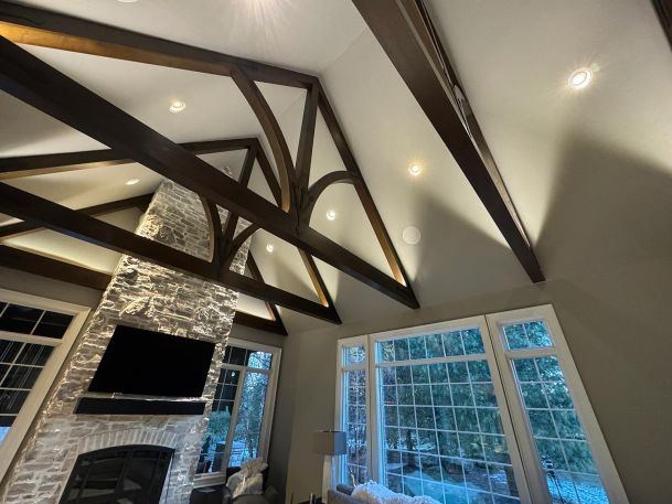 Vaulted ceiling with dark wood trusses and recessed can lighting above large window