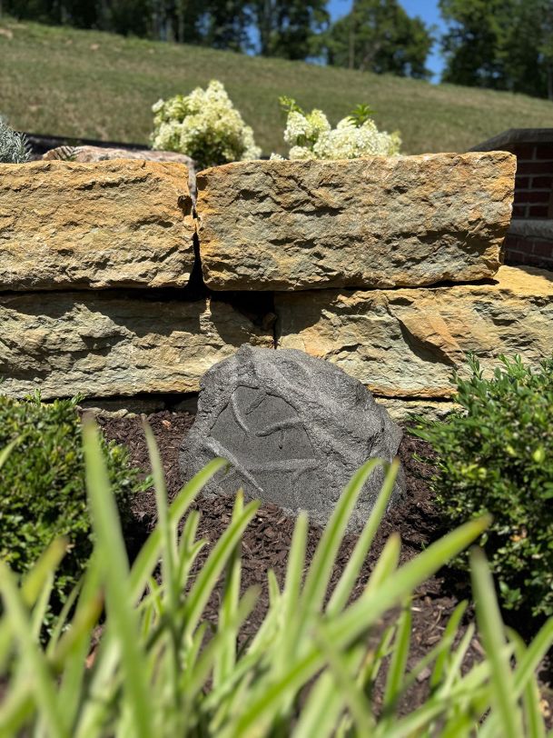 Exterior rock audio speaker placed on mulch bed below stacked stone terrace walls