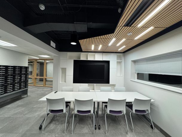 Conference room showing white tables and chairs below a decorative wood slat ceiling panel