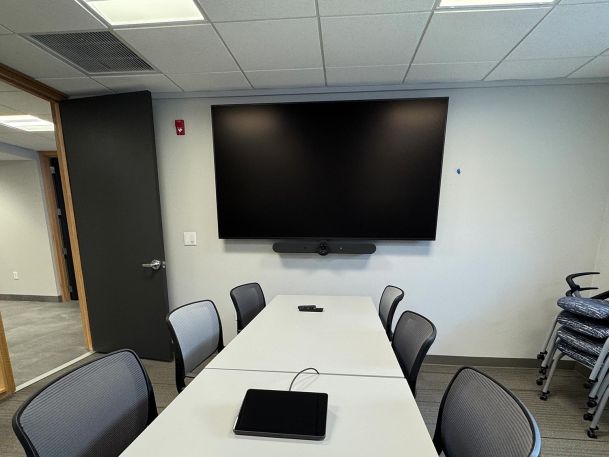 Corporate meeting room with long white table and wall mounted video display monitor