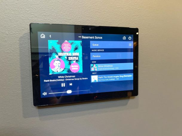 Smart home automation touchscreen displaying music playback menu options mounted on a wall