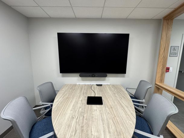 Office conference room showing oval table with central control screen and wall television