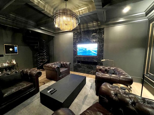 Dark moody den with tufted leather sofas and television screen mounted on black marble wall