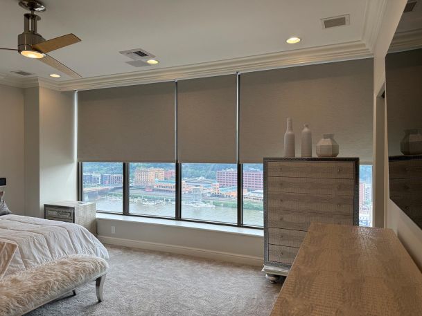 Bedroom window wall featuring three large roller shades covering glass panels over river view