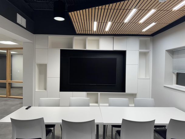 Modern boardroom featuring white built in shelving around a large black display screen