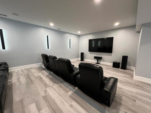 Home theater room featuring black leather recliners and wall mounted television with speakers