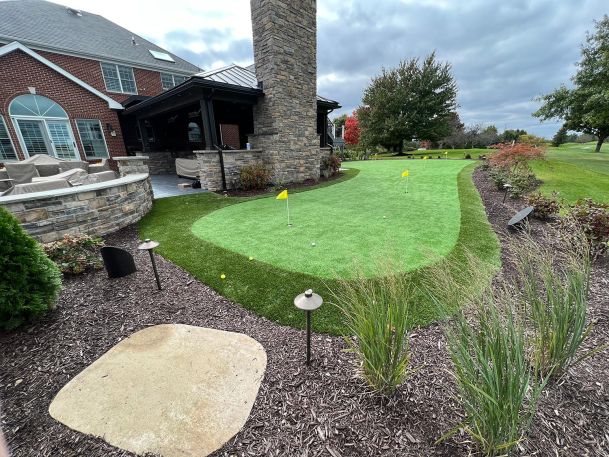 Wide view of residential brick home showcasing custom back lawn putting green landscaping