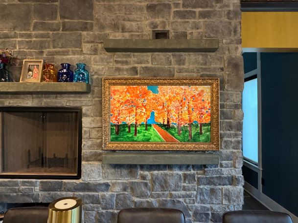 Bright orange landscape oil painting framed on a gray stone wall over stone mantel ledge
