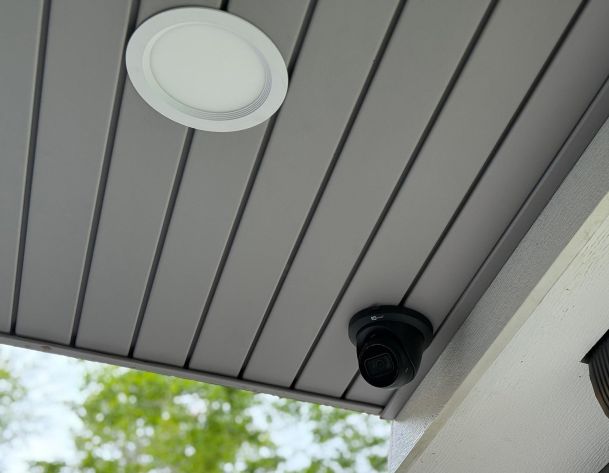 White circular recessed light panel and black security camera installed on gray slat ceiling