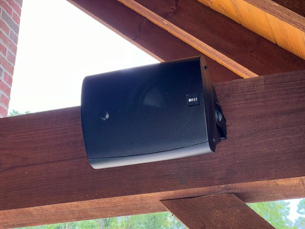 Black weather resistant outdoor speaker bracket mounted to a thick dark wood structural beam