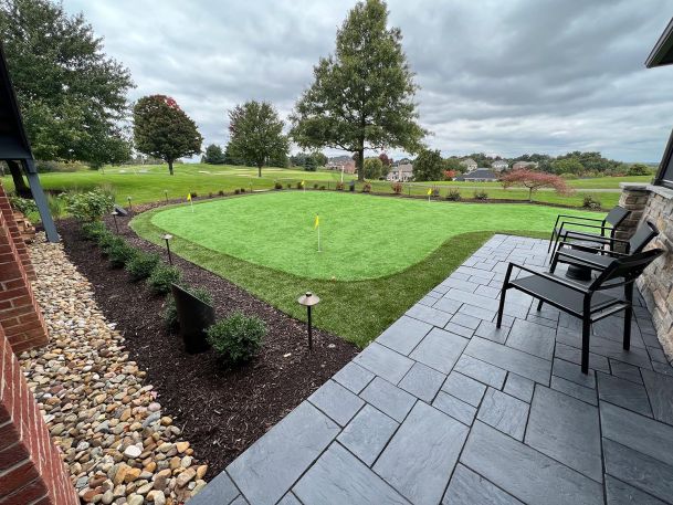 Outdoor backyard synthetic putting green with flags seen from a flagstone patio terrace