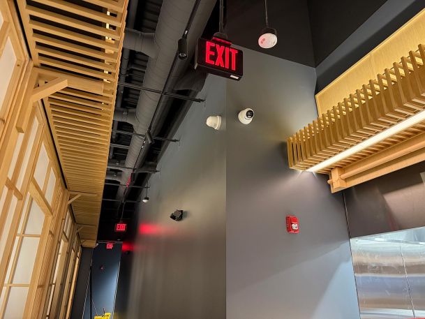 Illuminated red exit sign and white dome security cameras mounted on dark hallway wall