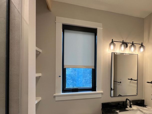 Bathroom window equipped with a single dark motorized window roller shade treatment