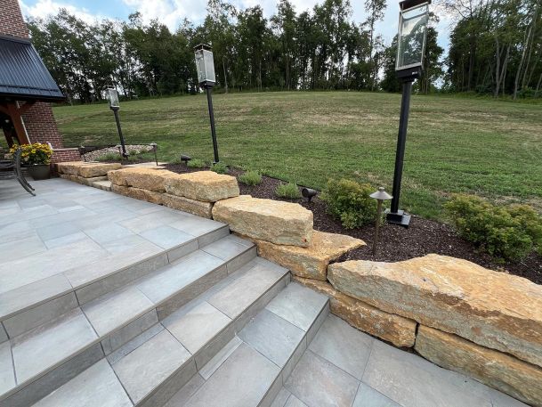 Tile patio walkways flanked by stone walls showing black exterior lighting pillars