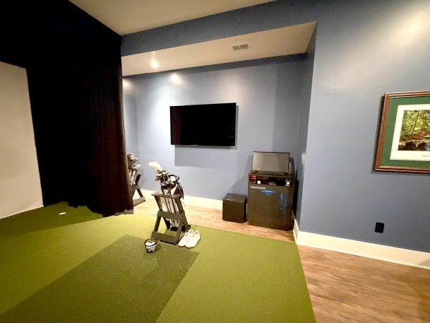 Room overview of golf tracking monitor station with club bag stand and side display monitor