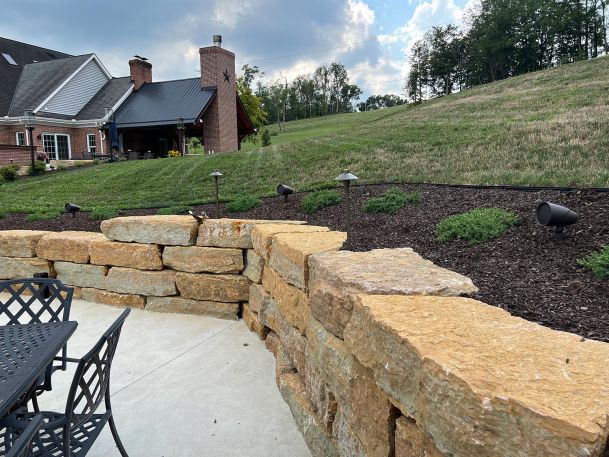 Landscaped mulch bed with outdoor pathway lights and directional spot speakers behind stone wall
