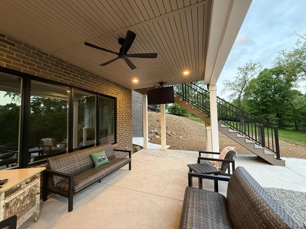 Covered concrete patio with outdoor seating and a ceiling mounted television display screen