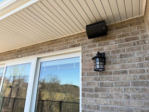 Black outdoor wall lantern lantern next to black wall speaker under soffit ceiling