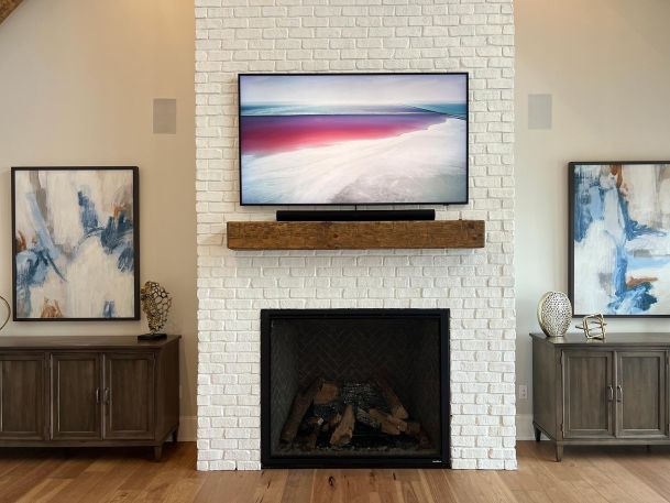 Flat screen television displaying abstract art over white brick fireplace with wooden mantel