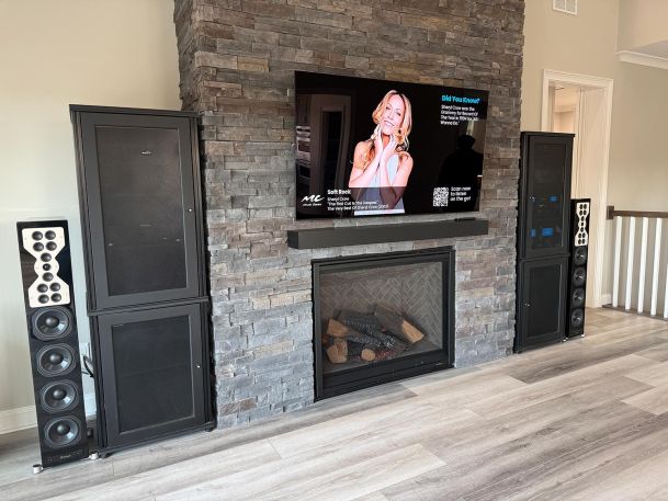 Flat screen television mounted on stone fireplace with tower speakers on wood floor