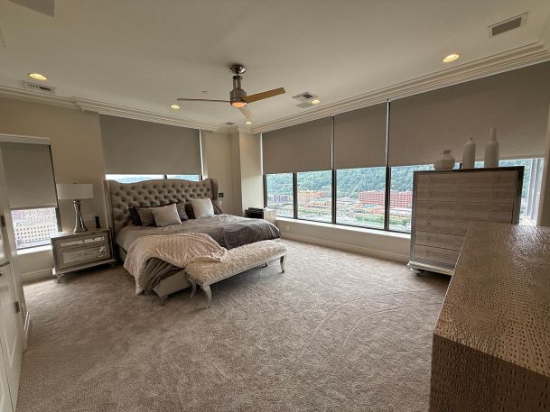 Luxury master bedroom with large windows covered by neutral colored roller window shades