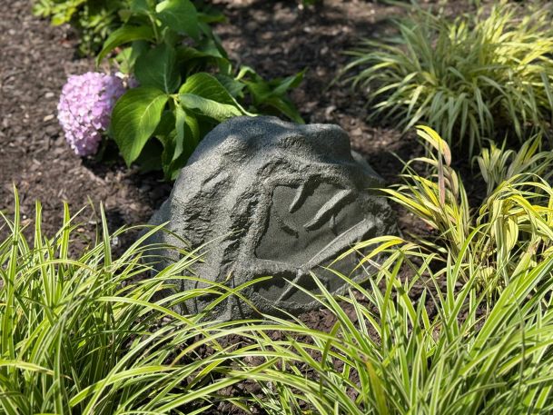 Close up of a rock shaped outdoor landscape speaker in a flower bed next to green grass